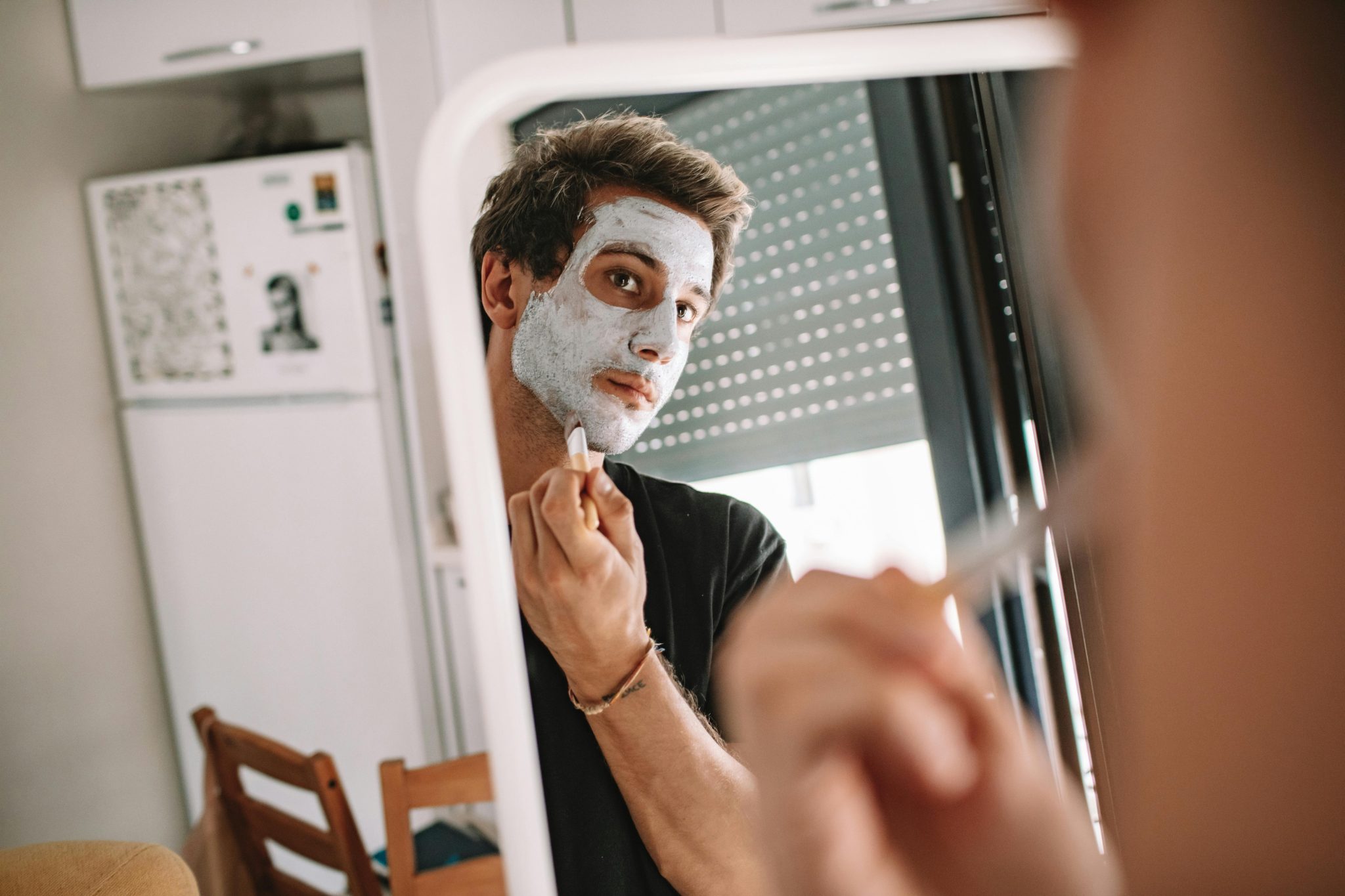 A man applying a face mask while looking into a mirror, emphasizing self-care and grooming.