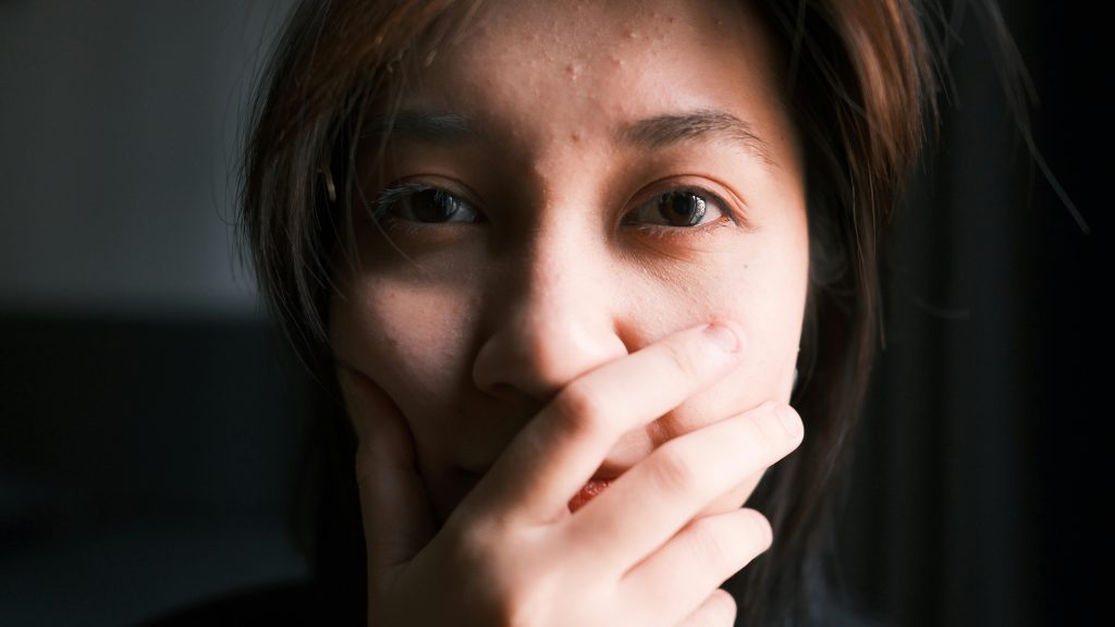 A thoughtful close-up portrait of a person covering their mouth with a hand, expressing emotion.