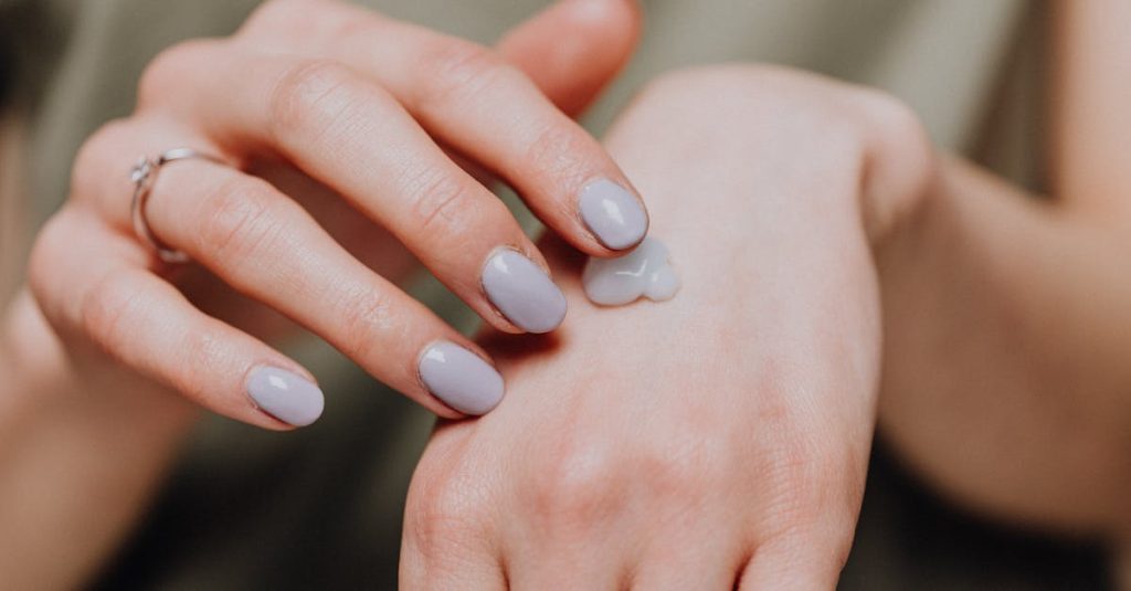 Crop unrecognizable female in casual shirt with trendy manicure and ring rubbing hand cream in back of hand skin